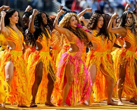 Shakira and a row of dancers in orange outfits